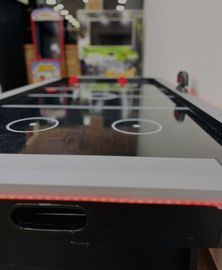 Mesa de air hockey com iluminação vermelha e fliperamas ao fundo